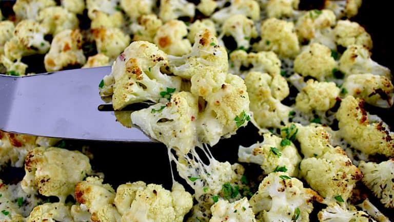 Cheesy Roasted Cauliflower being held up by silver spatula with cheese pull