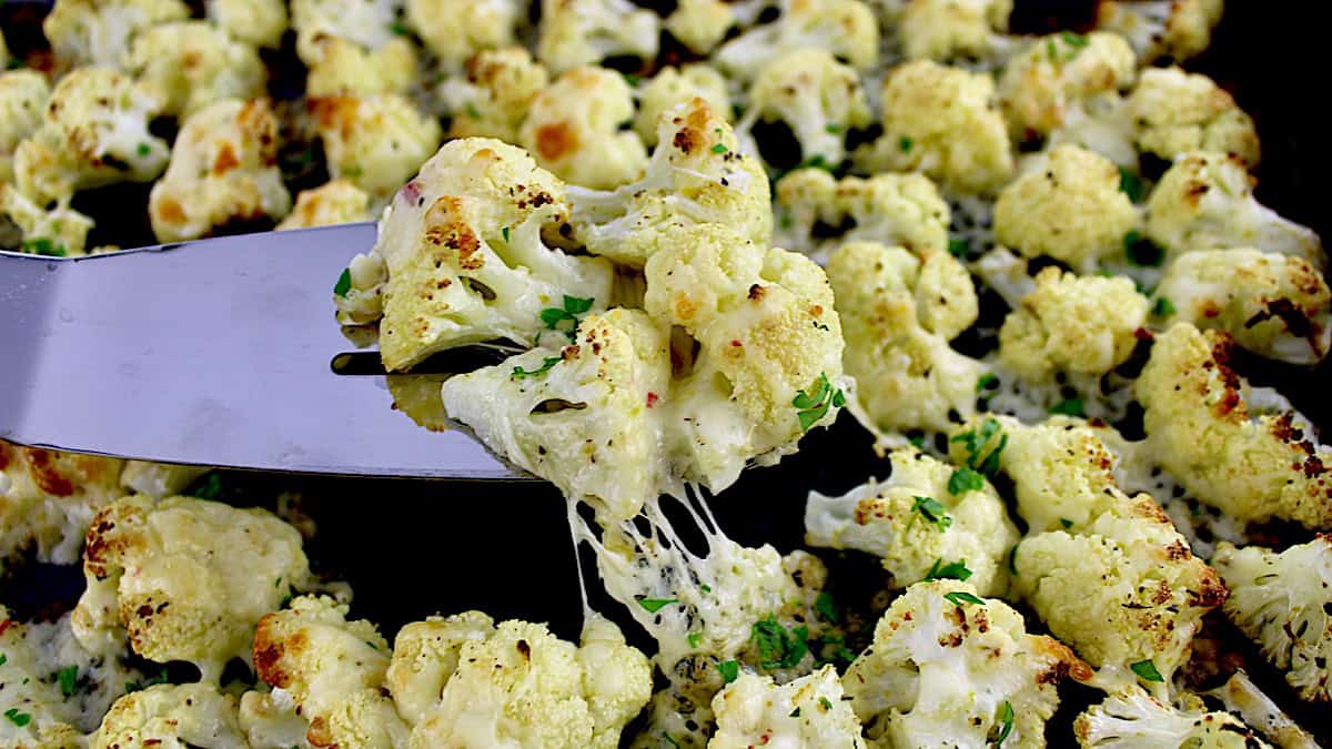 Cheesy Roasted Cauliflower on sheet pan with silver spatula lifting up some with cheese pulling