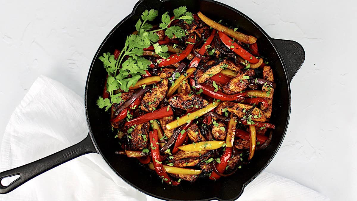 Chicken Fajitas in cast iron skillet with fresh cilantro on side