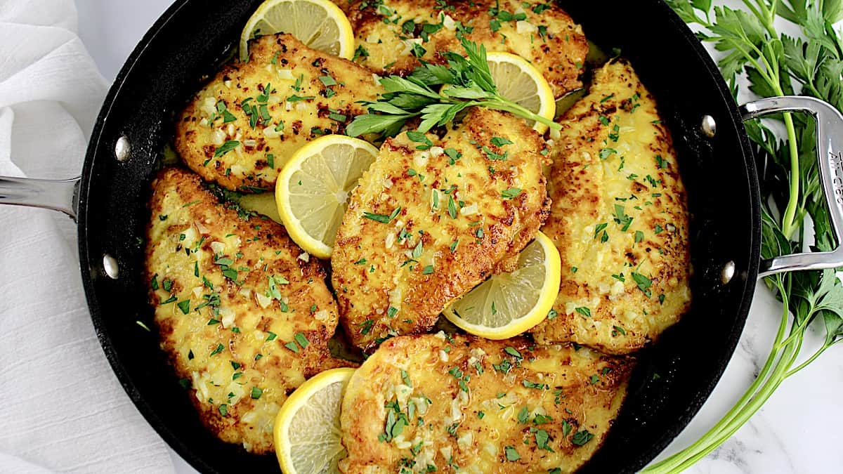 closeup of Chicken Francese in skillet with lemon slices and parsley garnish