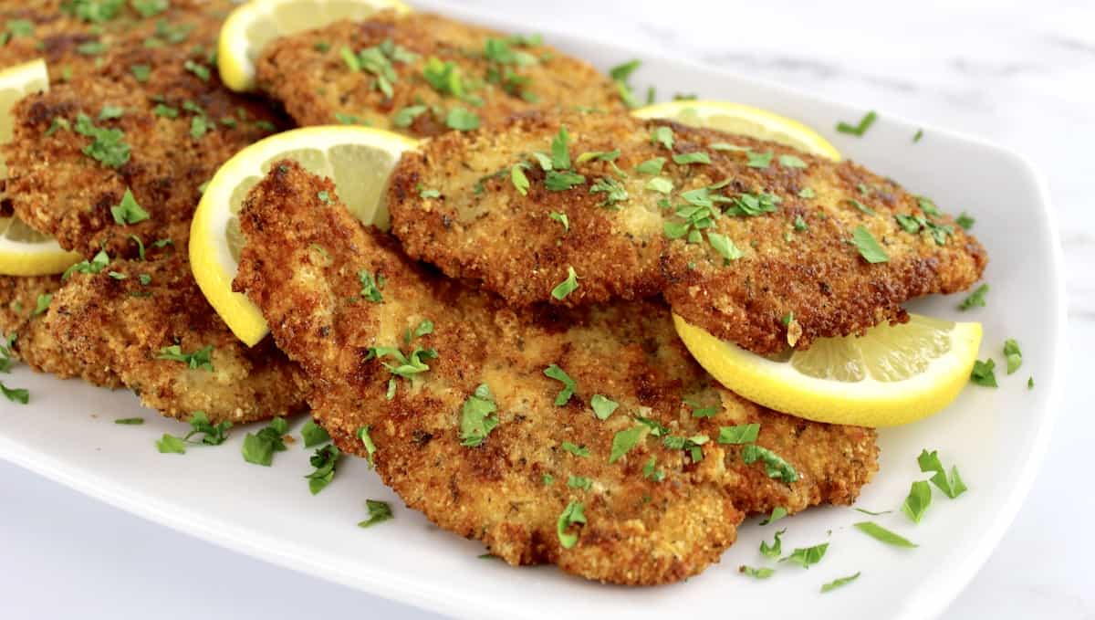 Chicken Milanese on white plate with lemon slices and chopped parsley