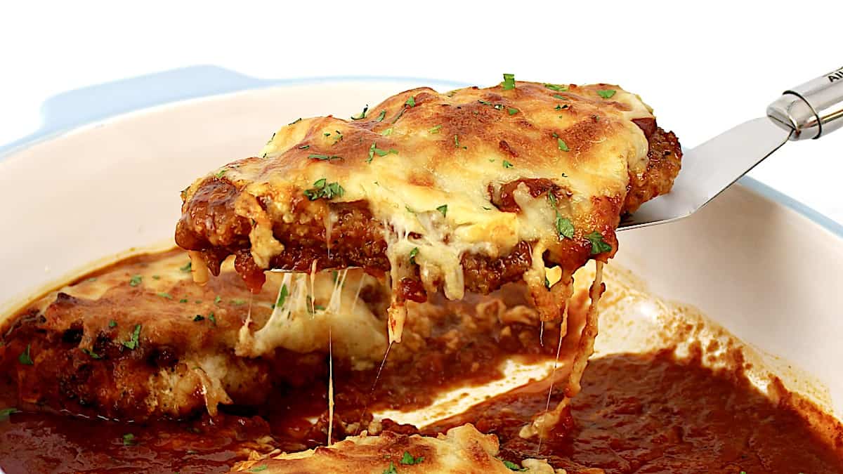 Chicken Parmesan piece being held up by silver spatula with cheese pull