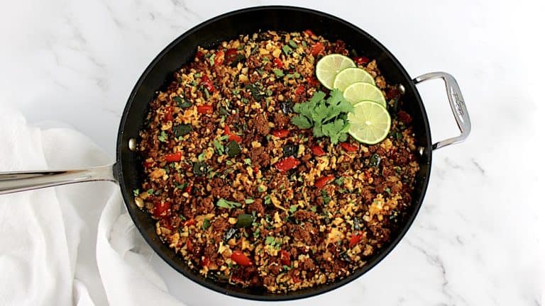 Chorizo Cauliflower Rice in skillet with 4 lime slices and cilantro garnish