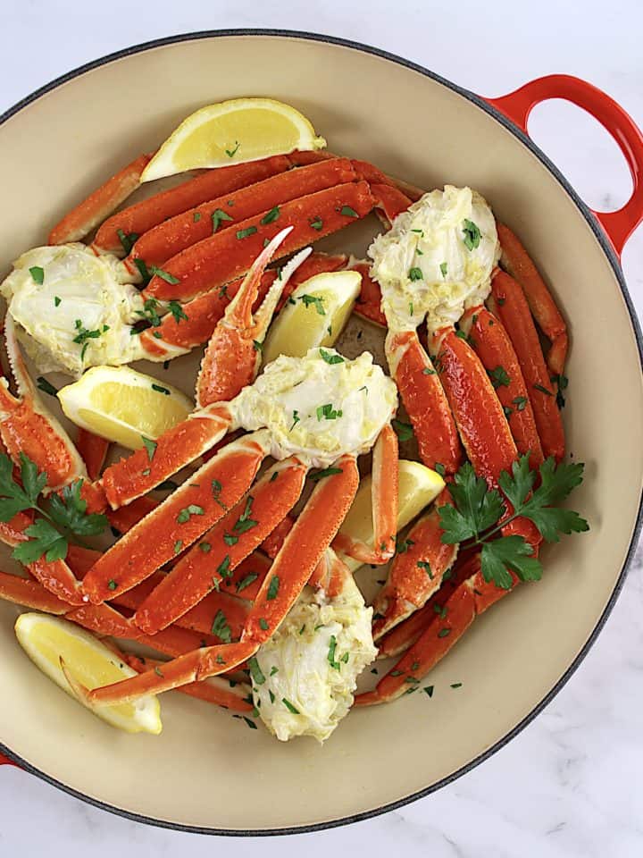 Crab Legs with Garlic Butter in skillet with lemon wedges and parsley