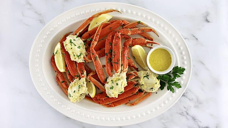 Crab Legs with Garlic Butter on white platter with lemon wedges and garlic butter in white bowl