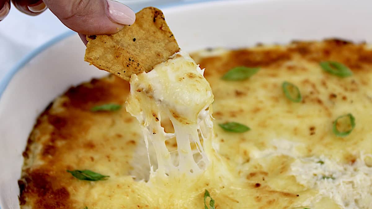 Crab Rangoon Dip with chip being dipped in pulling the cheese