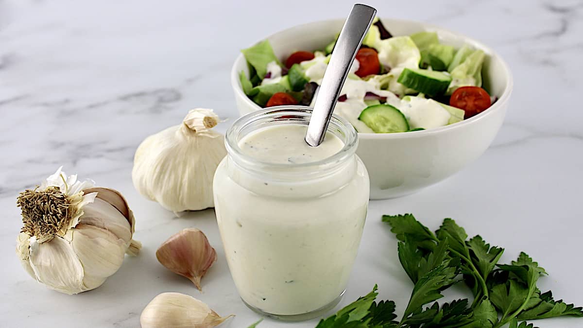 Creamy Garlic Italian Dressing in glass jar with spoon in it with salad in background