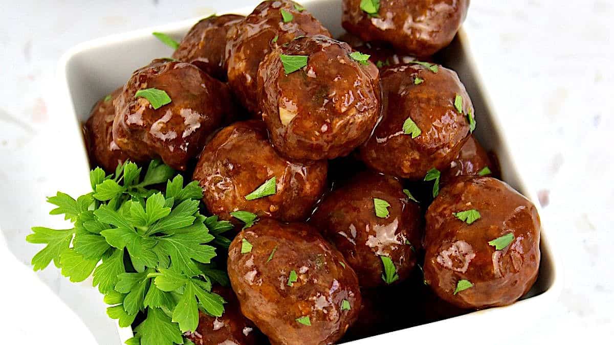 Slow Cooker BBQ Meatballs piled up in white bowl with fresh parsley garnish