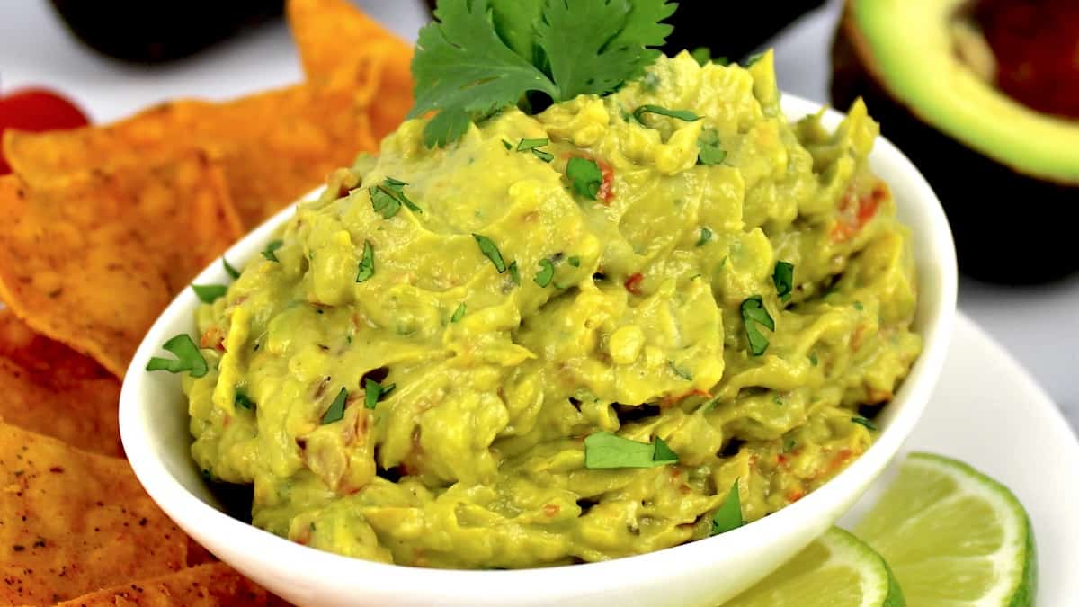 easy guacamole in white bowl with cilantro sprig on top