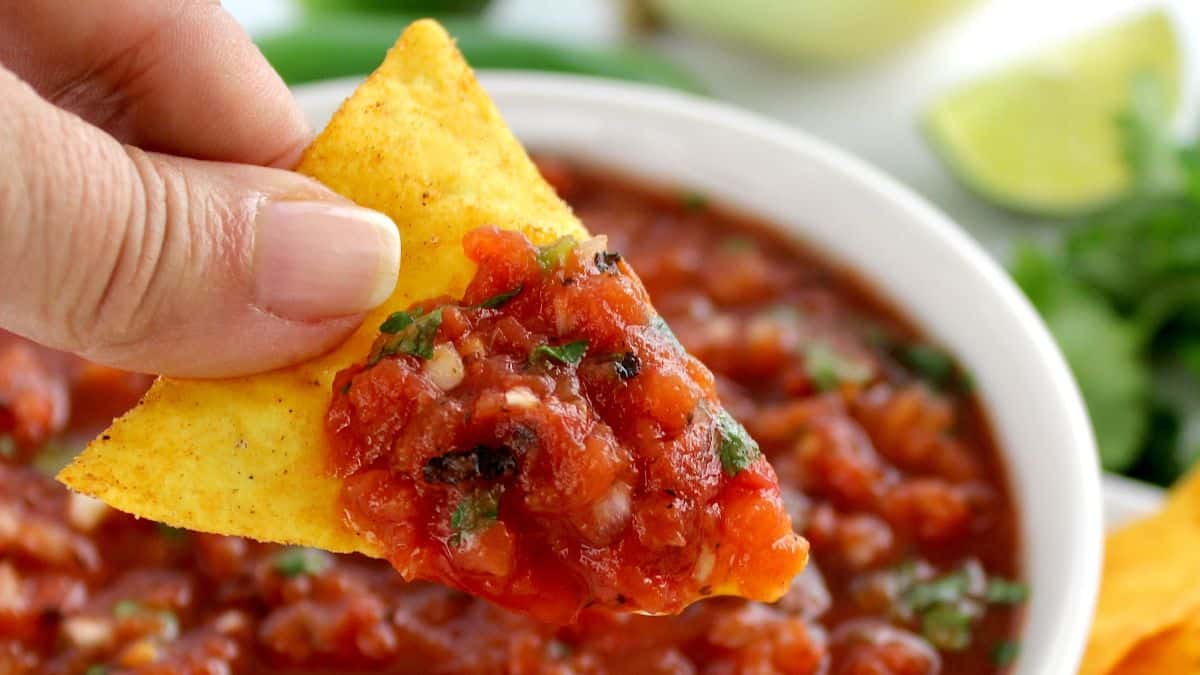 hand holding up tortilla chip with Easy Homemade Salsa on top