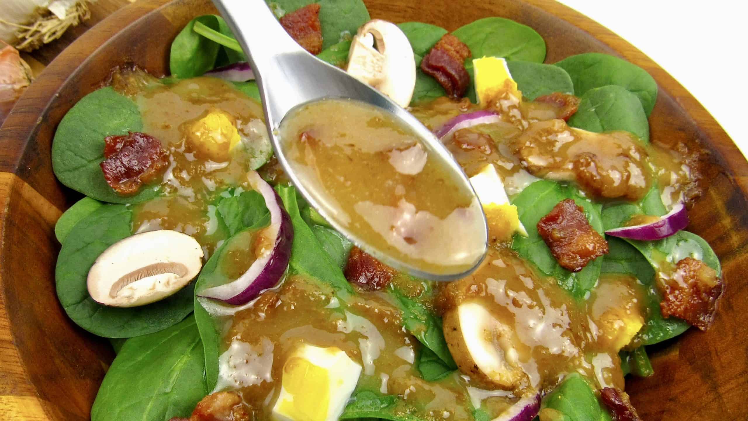 spoonful of hot bacon dressing over spinach salad