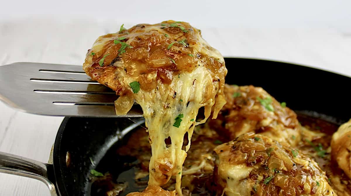 French Onion Chicken piece held up by silver spatula with cheese pull