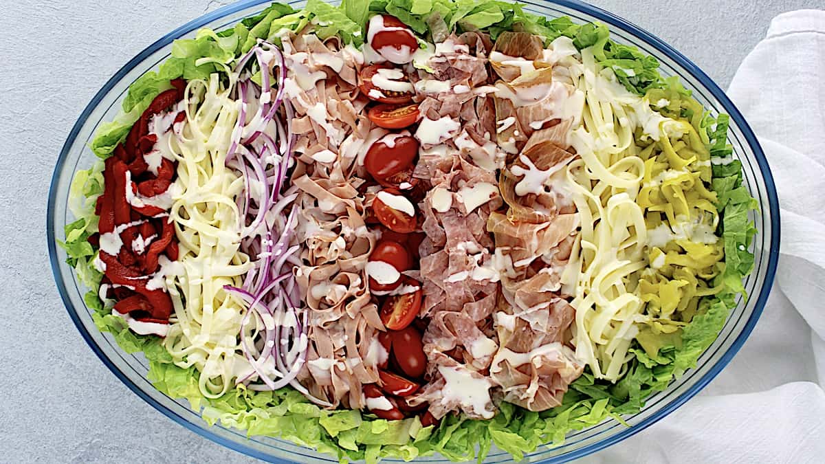 Grinder Salad in oval glass bowl with ingredients arranged in vertical rows over lettuce