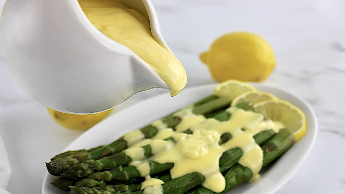 Hollandaise Sauce being poured over asparagus on white plate