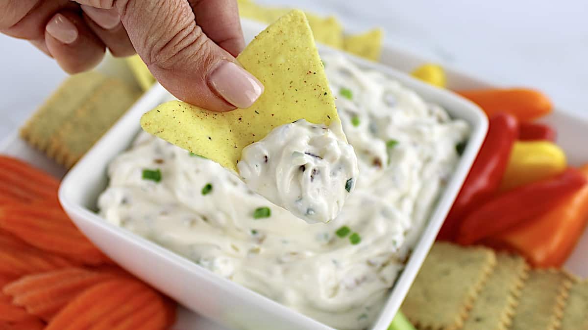 french onion dip in white bowl with tortilla chip dipping in