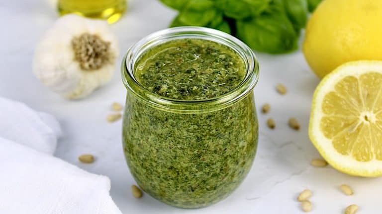 Homemade Pesto Sauce in open glass jar with basil, garlic and lemon in back