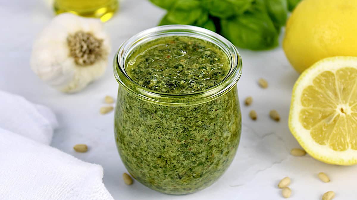 Homemade Pesto Sauce in open glass jar with basil, garlic and lemon in back