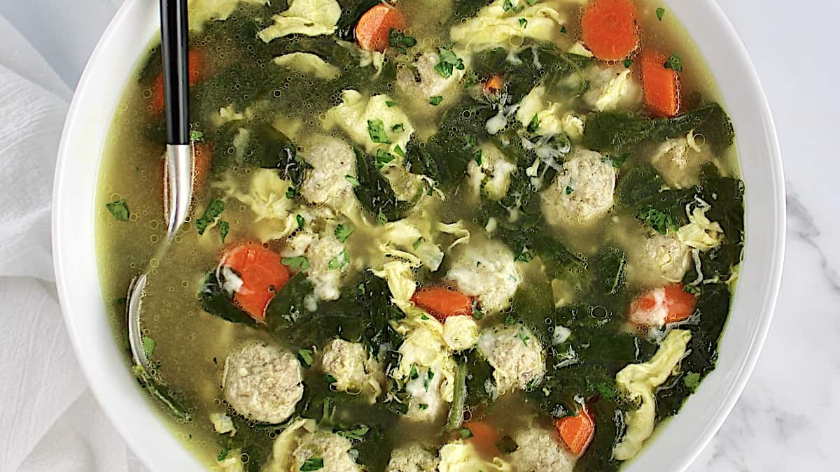 Italian Wedding Soup with grated cheese on top and spoon in the bowl