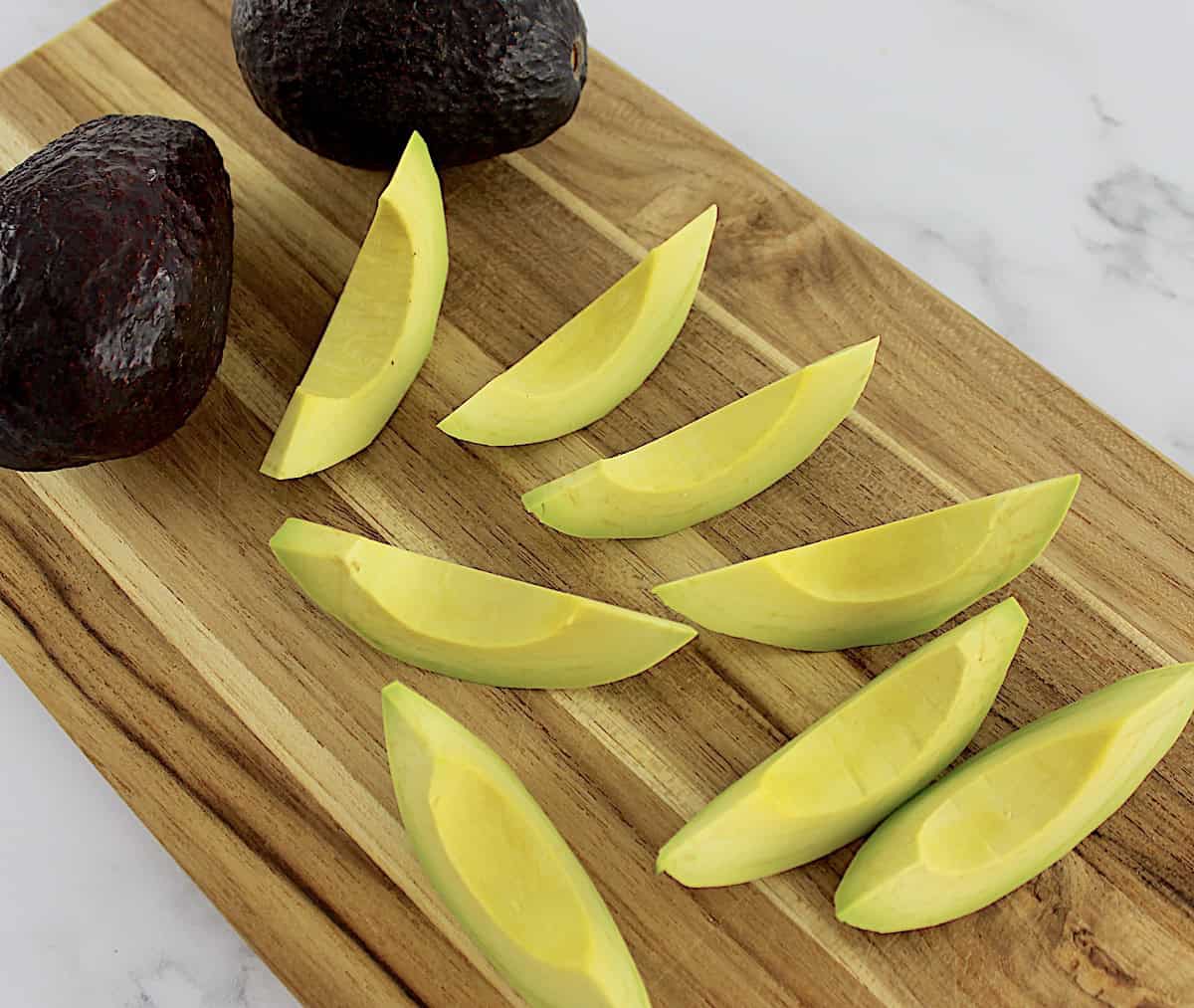 fresh avocados with one cut into wedges on cutting board