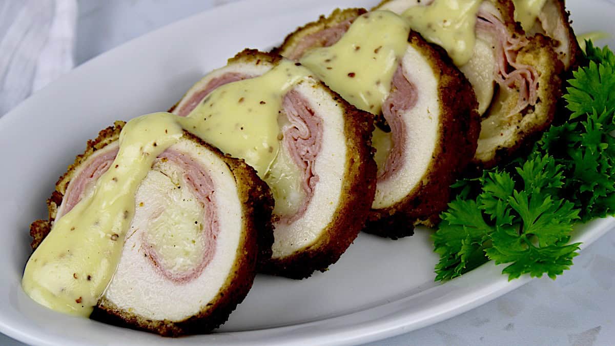 Keto Chicken Cordon Bleu sliced on white plate with cheesy mustard sauce drizzled on top