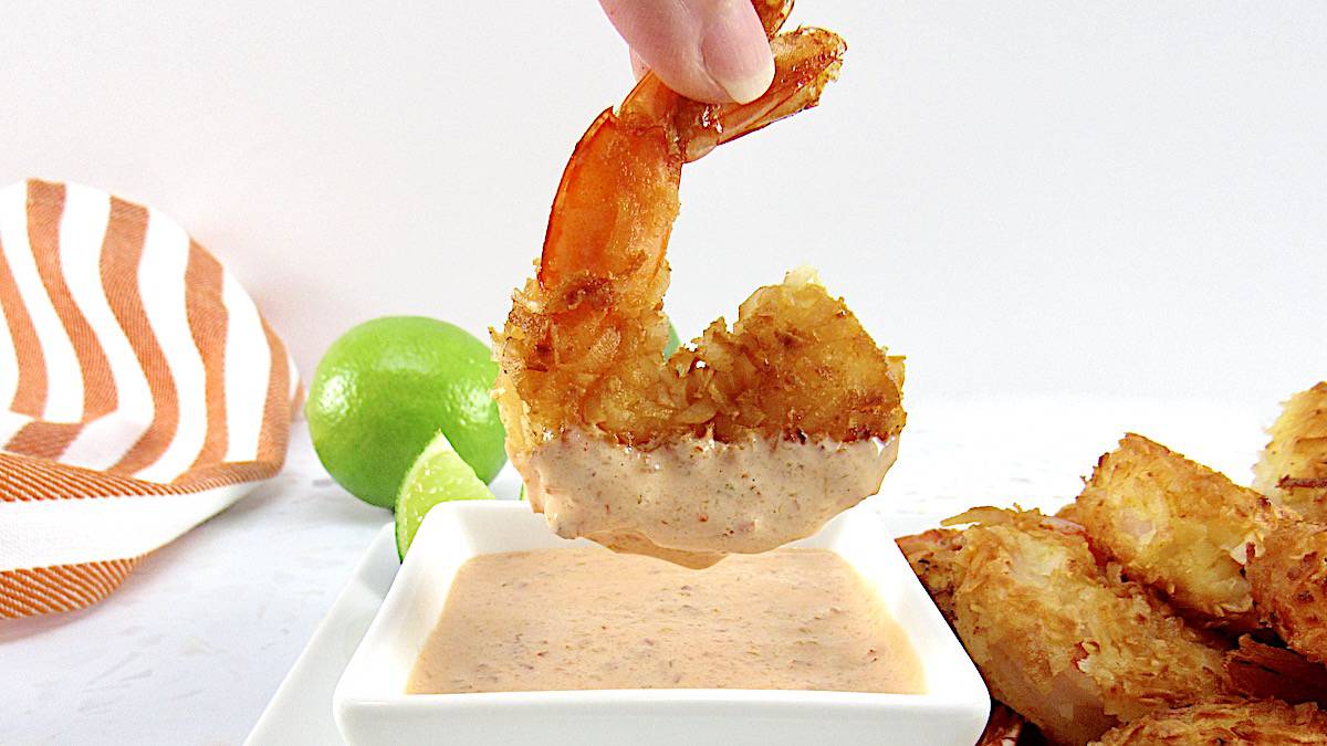 Keto Coconut Shrimp being dipped in sauce in white bowl
