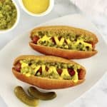 2 Keto Hot Dog Buns with hot dogs, mustard and relish with 2 pickles on side