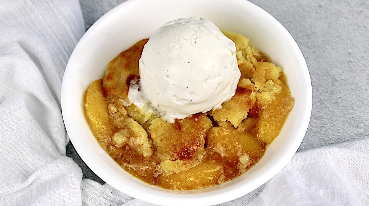 Keto Peach Cobbler in white bowl with scoop of vanilla ice cream on top