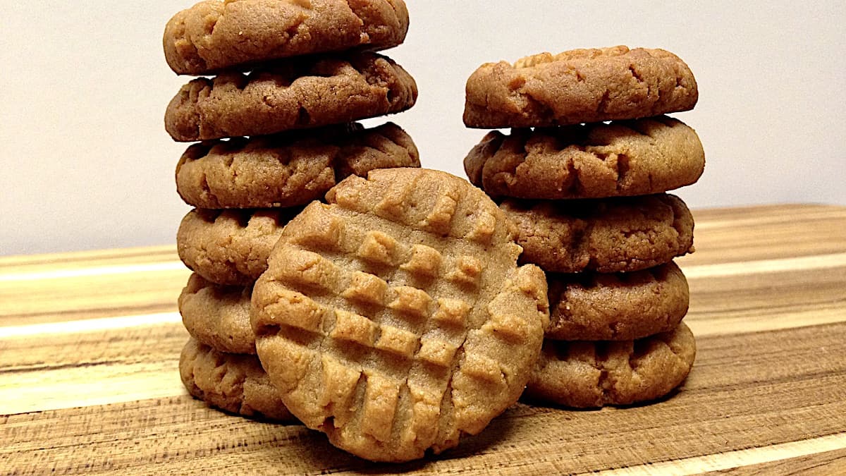 2 stacks of Keto Peanut Butter Cookies on cutting board with one cookie standing upright