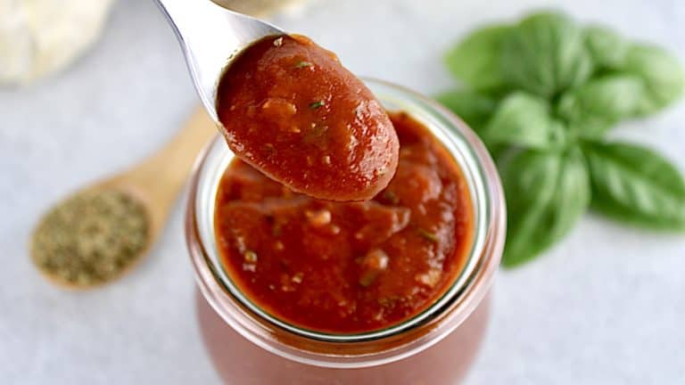 pizza sauce on a spoon over a jar filled with sauce