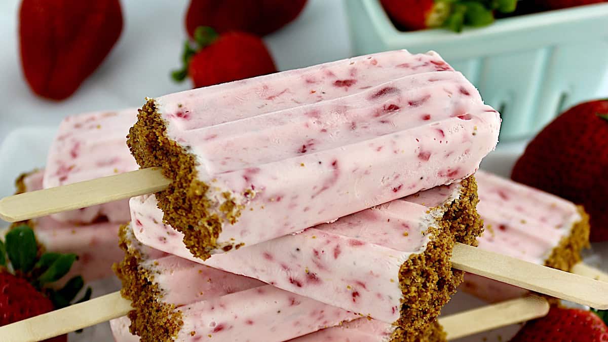 Keto Strawberry Cheesecake Popsicles stacked up with strawberries in back