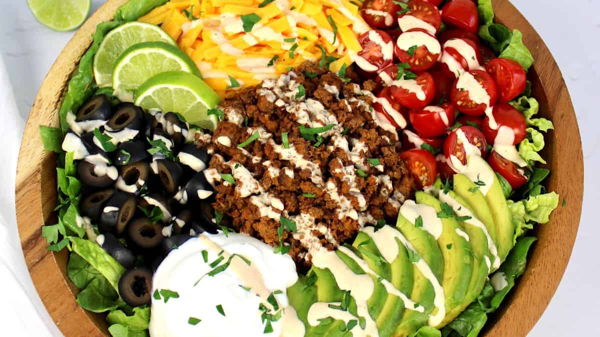 closeup of Keto Taco Salad in wooden bowl with dressing drizzled on top