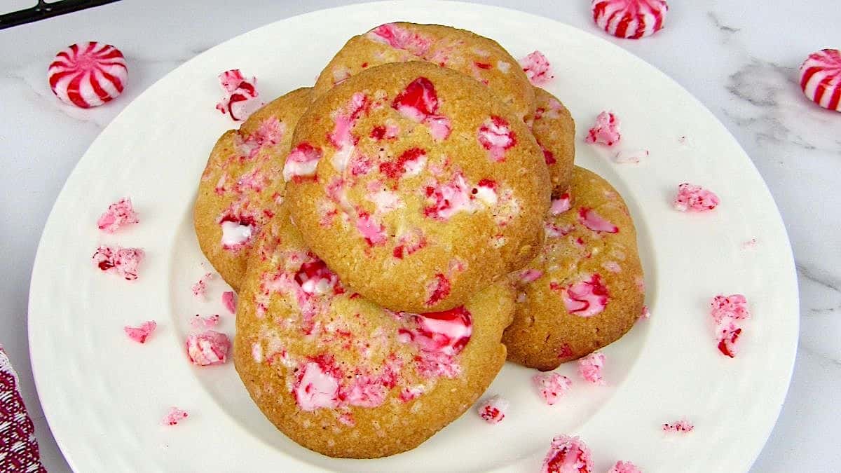 Keto white chocolate peppermint cookies stacked on white plate with peppermint candy pieces around
