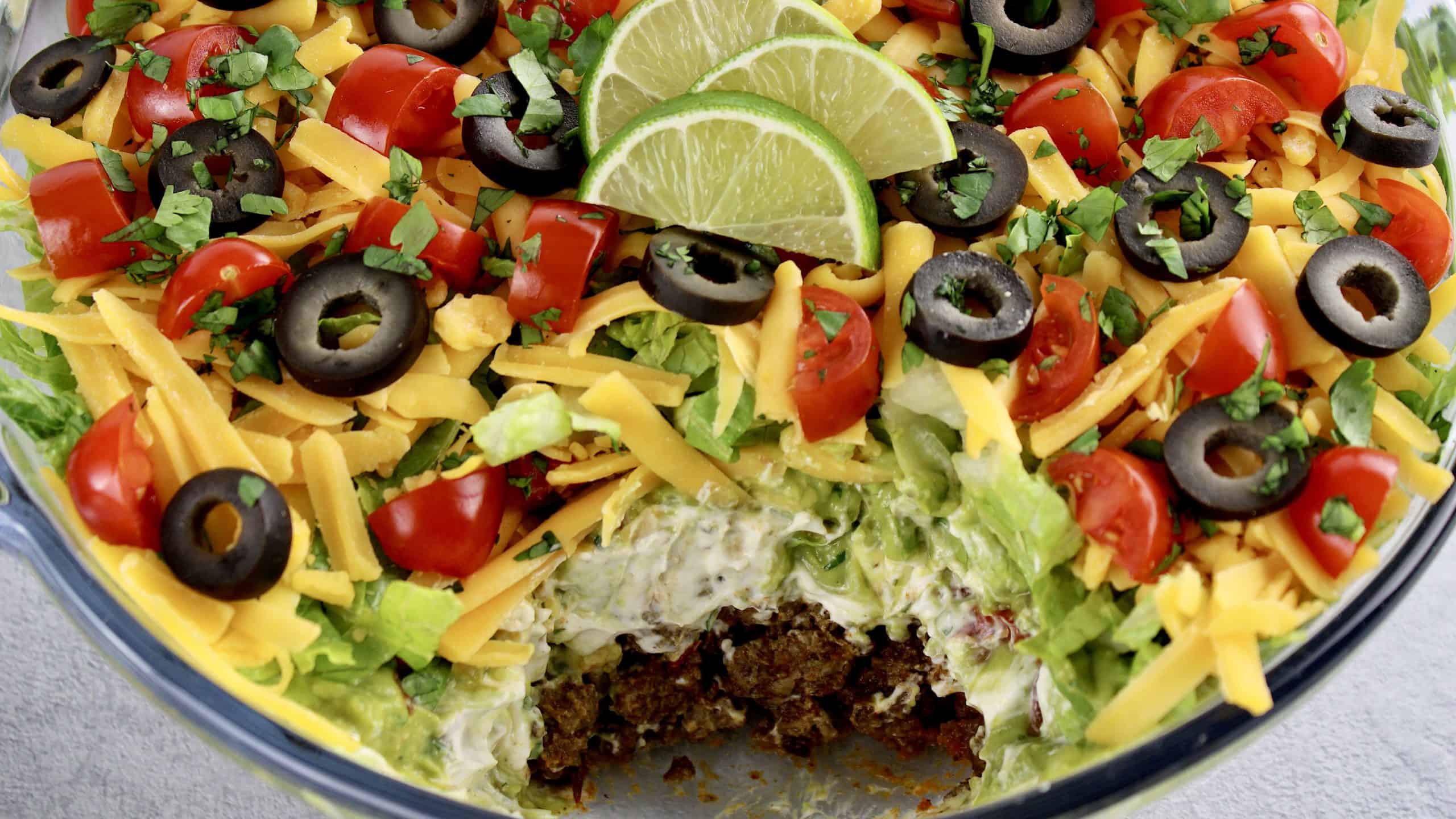 Layered Taco Dip with some missing and 3 lime slices on top