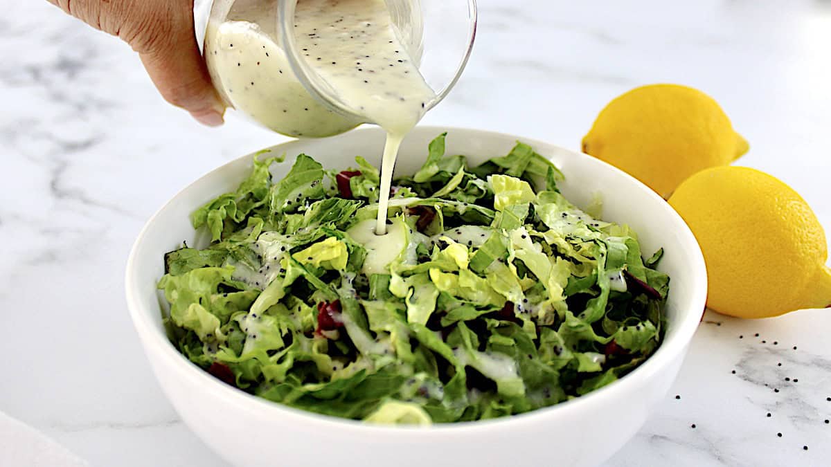 Lemon Poppy Seed Dressing being poured over salad in white bowl