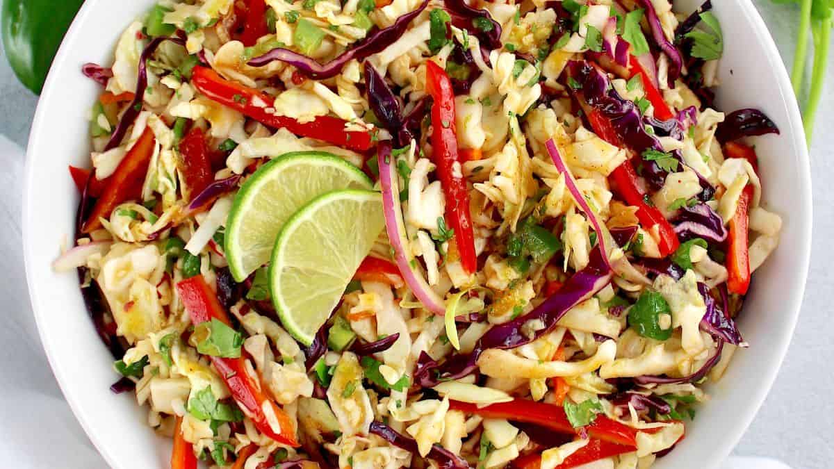 closeup of Mexican Coleslaw in white bowl with 2 lime slices on top