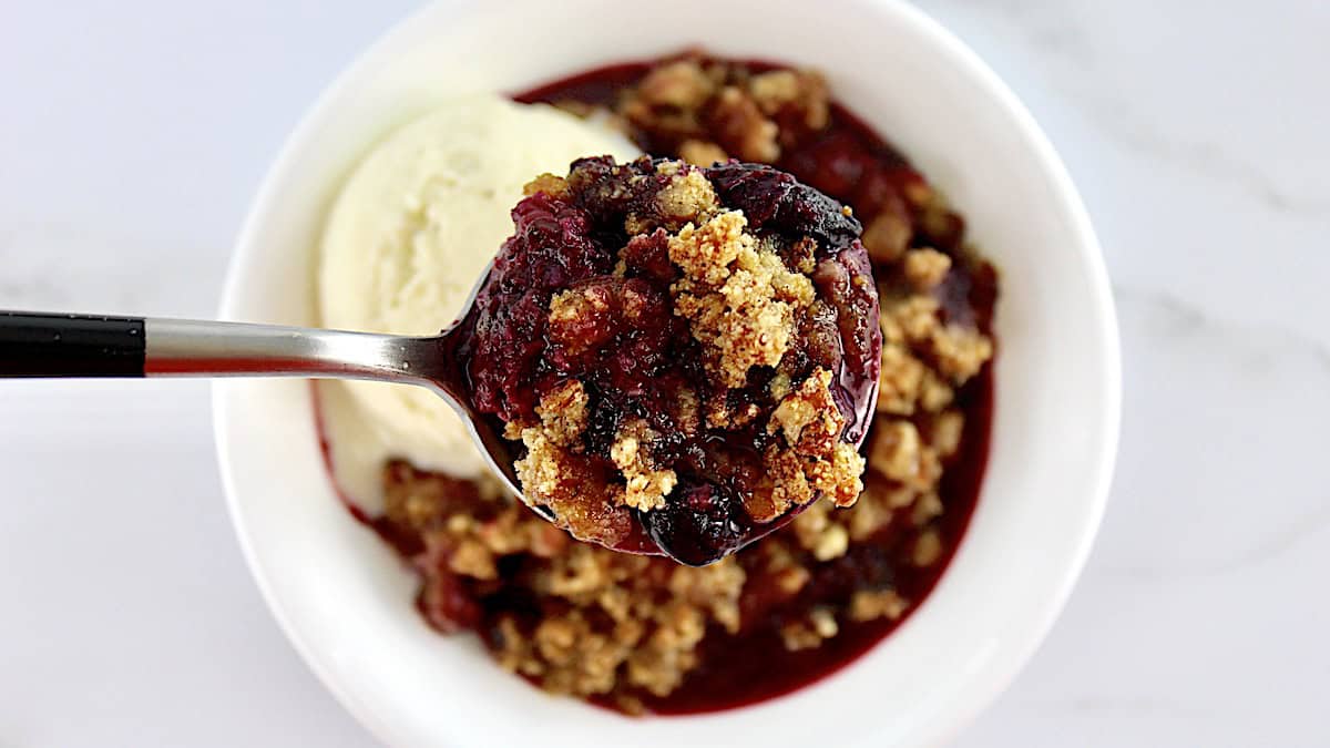 Mixed Berry Crumble with vanilla ice cream and spoon holding up some