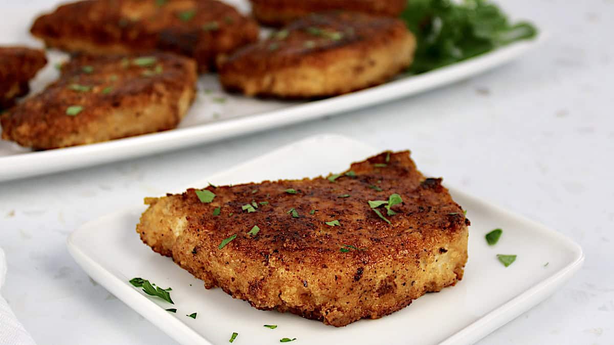 closeup of pan fried pork chop on white plate with more in background