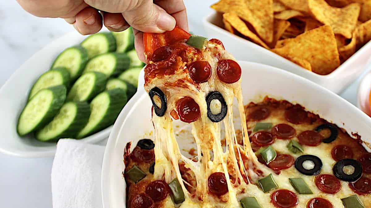 red bell pepper dipping into pizza dip and pulling up cheese