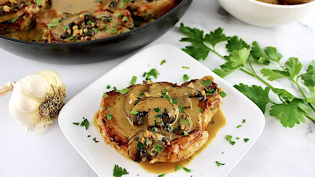 Pork Marsala piece on white square plate with chopped parsley and skillet in background