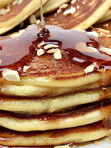 stack of Ricotta Almond Pancakes on white plate with syrup being poured over top