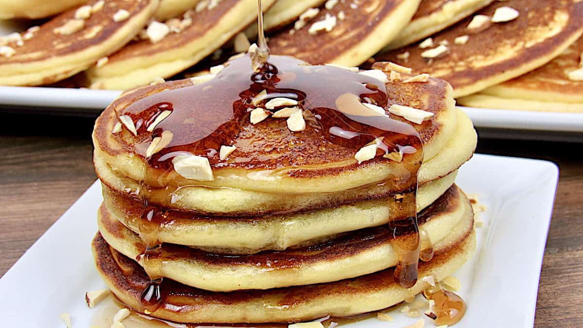 stack of Ricotta Almond Pancakes on white plate with syrup being poured over top