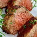 closeup of slices of Roast Beef Tenderloin on white plate with fresh rosemary