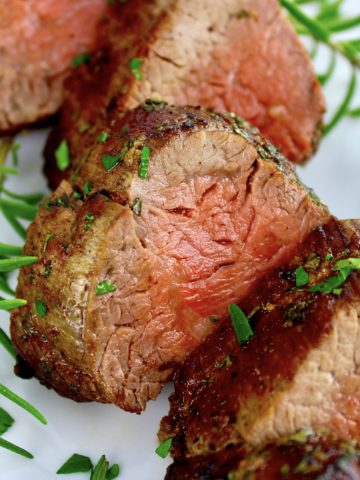 closeup of slices of Roast Beef Tenderloin on white plate with fresh rosemary