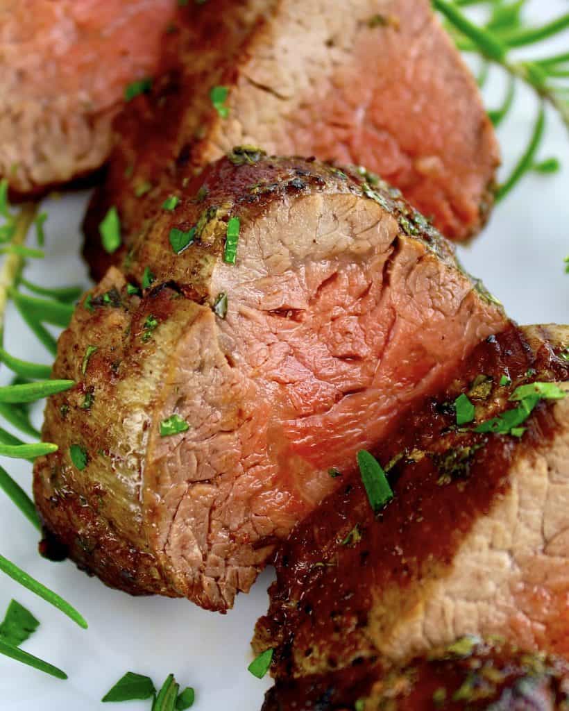 closeup of slices of Roast Beef Tenderloin on white plate with fresh rosemary