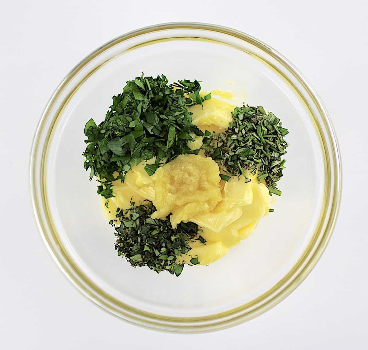 herbs, grated garlic and butter in glass bowl unmixed