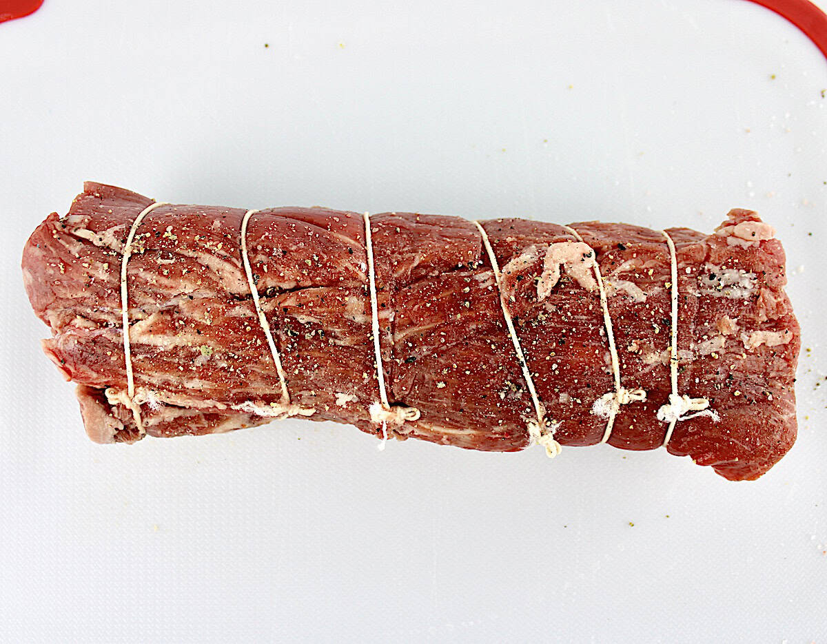 beef tenderloin on white cutting board tied up with kitchen twine