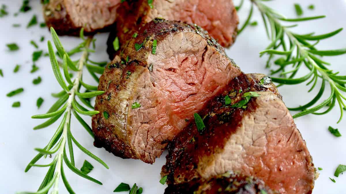 Roast Beef Tenderloin slices on white plate with fresh thyme and rosemary