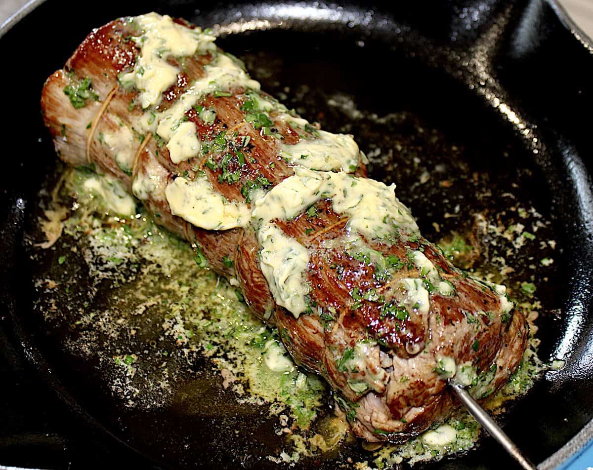 Roast Beef Tenderloin in skillet with meat thermometer probe and herb butter slathered all over