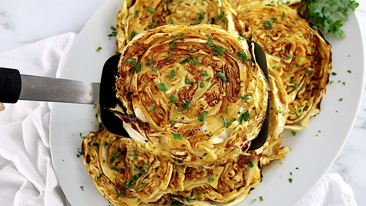 Roasted Cabbage Steak being held up with spatula with chopped parsley on top