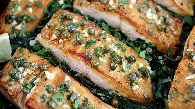 Salmon Piccata in skillet over fresh spinach with capers on top